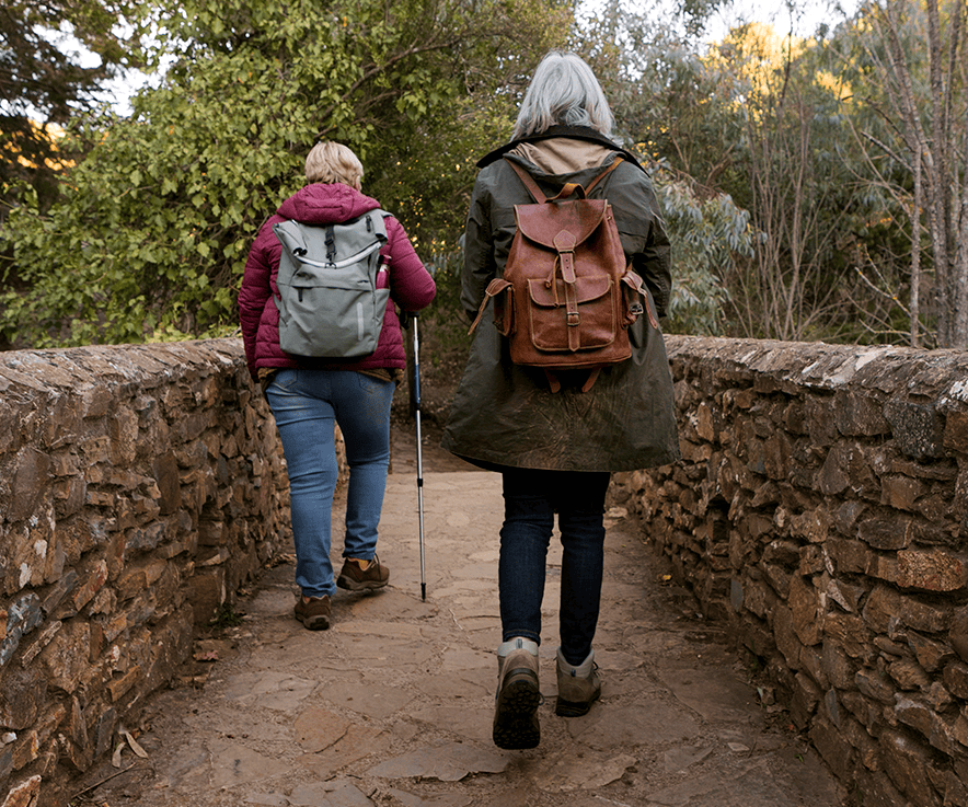 hero_0000_dos-mujeres-mayores-cruzando-un-puente-de-piedra-mientras-estan-en-la-naturaleza